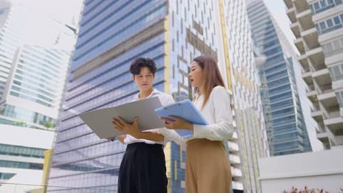 Asian young businessman and woman partner working outdoors in the city.