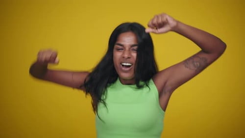 Smiling Female Model Jumping Excitedly Celebrating a Victory on Yellow Background in Studio