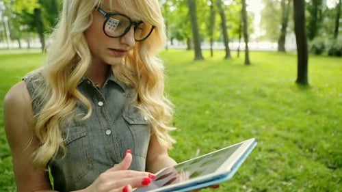 Closeup Portrait of Happy Young Blonde Woman Using Tablet Pc in the Park