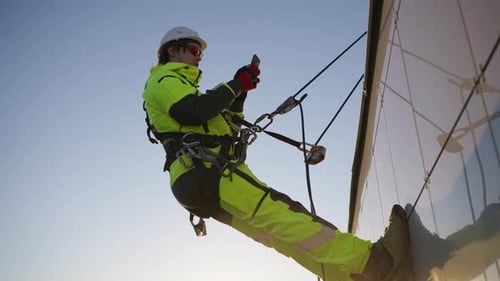 Homem, alpinista industrial em equipamento e capacete, é amarrado com uma corda a um prédio com uma entrada de telefone