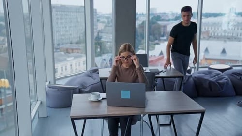Männlicher Angestellter kommt an den Tisch seiner Kollegin. Kollegen schauen beim Reden auf den Laptop-Bildschirm