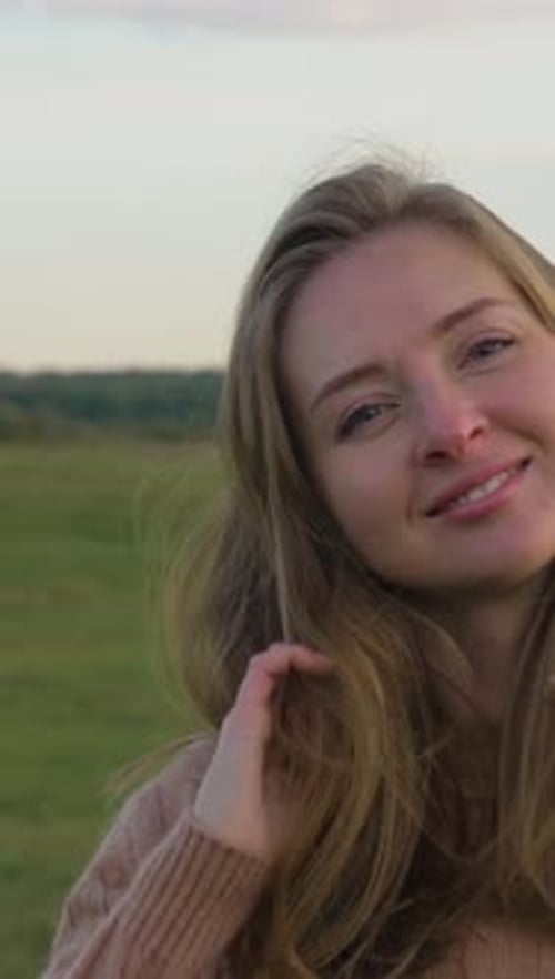 Portrait of Young Cheerful Woman Smiling and Touching Her Hair in Green Field Medium Shot Vertical