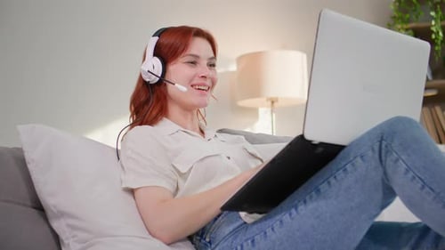 Smiling Woman Using Laptop and Headset on Couch