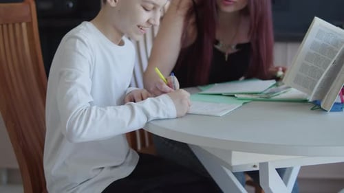 Teenager Writes with Assistance at Table Indoors