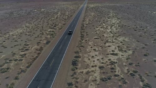 Slow motion, high, downward aerial view of a truck driving away on a straight, narrow desert highway