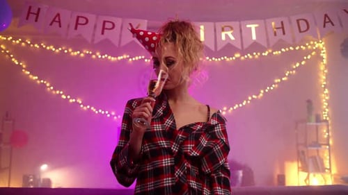 A Sad Crying Woman in a Birthday Cap Touching Her Head and Drinking Champagne