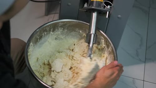 Industrial mixer for kneading dough in hands kitchen worker, mixing equipment in bakery.