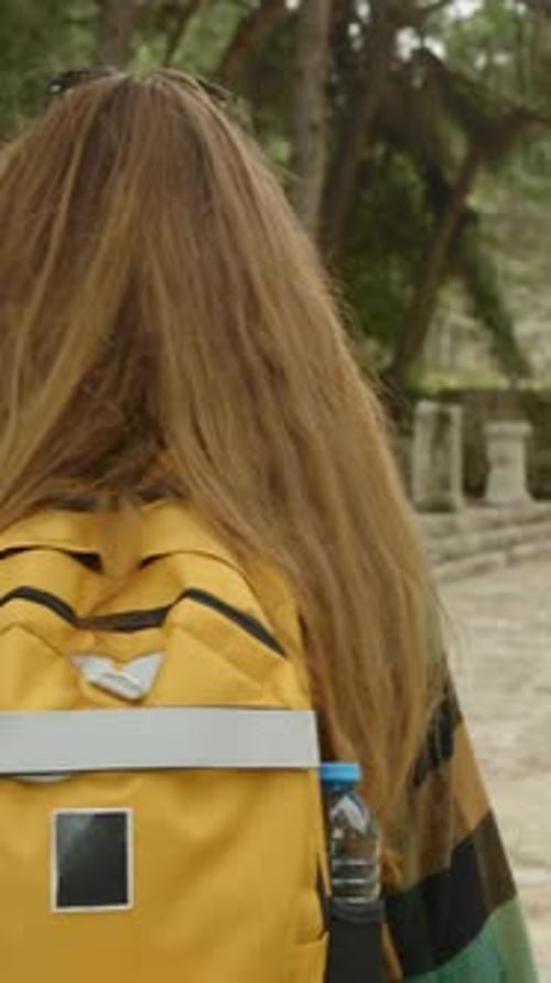 Vidéo verticale. Vue de derrière d'une jeune touriste avec un sac à dos lumineux qui marche.