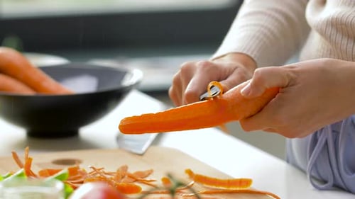 Woman peels and cuts carrots in kitchen