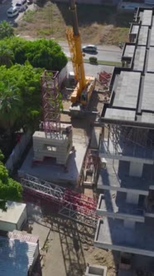 Vídeo vertical capturado por ingenieros expertos que construyen una grúa torre en un vibrante sitio de construcción