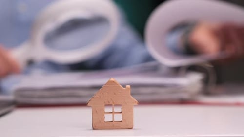 Architect Reviewing Plans with Miniature Wooden House in the Foreground