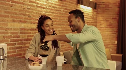 Homem negro cozinhando café da manhã na cozinha, esposa bebe café. Casal afro-americano, vida saudável