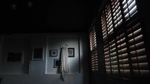 Wedding dress hanging on picture wall, lit by rays of shutter light