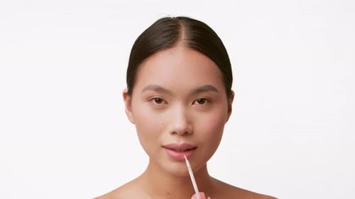 Young Woman Applying Lip Gloss While Pampering Herself in a Serene Setting