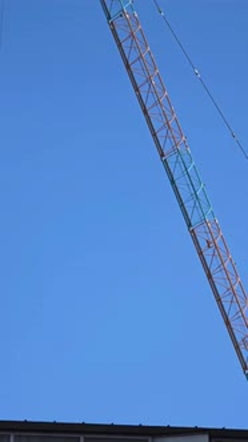 Close-up aerial shot moves along the steel lattice boom of a tower crane against a clear blue sky