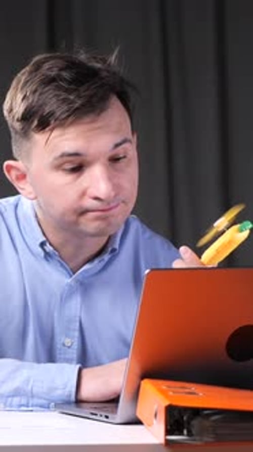 Vertical Video Man trabalha em um laptop no escritório e explode com um ventilador de mão