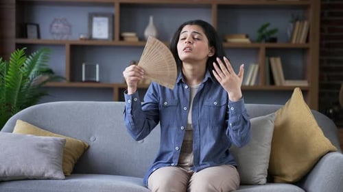 Woman Fanning Herself on Couch in Living Room