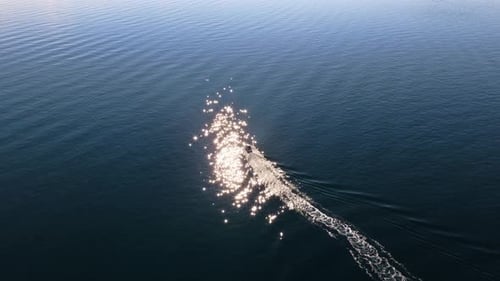 Aerial drone view of a small motorboat speeding across the water, leaving a white foamy trail behind