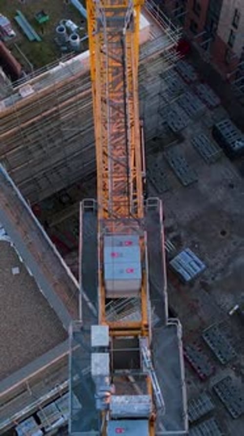 Portrait top-down drone shot of yellow crane over derelict urban construction site