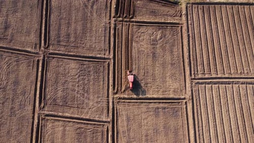 Aerial view of fields and agricultural parcels. Farmer in tractor preparing land with seedbed