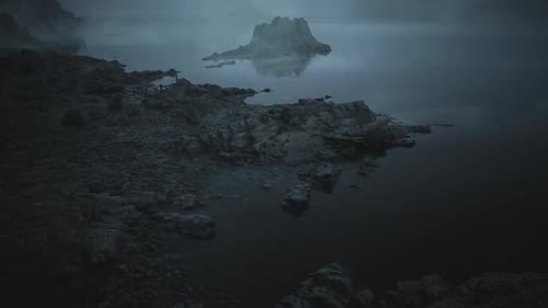 Misty Shoreline View with Rocky Island at Dawn Near Calm Water Body
