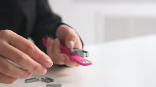 Hands Replacing Staples in a Small Pink Stapler on a White Office Desk