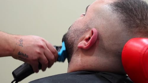 Tattooed hand trimming client's beard with trimmer