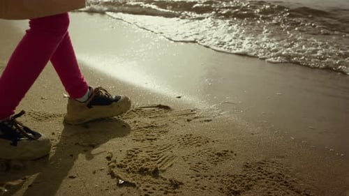 Little girl legs walking on sandy sea beach shoreline crashing waves