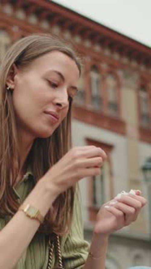 Young woman putting wireless earphone into ear on old city background
