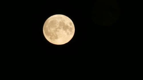 Glowing full harvest moon crater surface closeup passing across dark sky