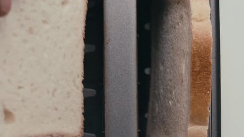 Close-Up View of Hand Inserting Bread Slices into Toaster