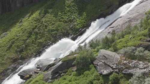 Slowmotion drone shot panning up to a powerful waterfall in Norway with strong current going down on