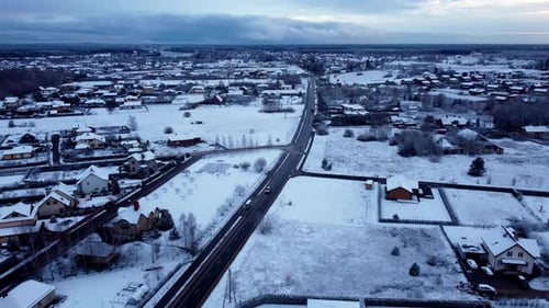 Aerial drone follows a vehicle driving through snow covered countryside village at sunset