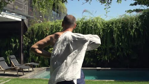 Man Putting on Shirt by Tropical Swimming Pool