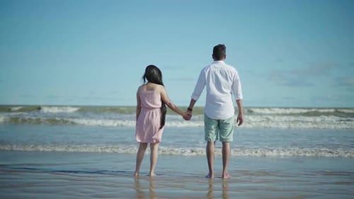 Slow motion shot of a couple in a beach standing and watching the beautiful waves