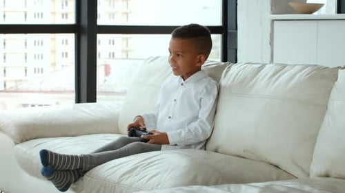 Young Boy Plays Video Game on White Sofa