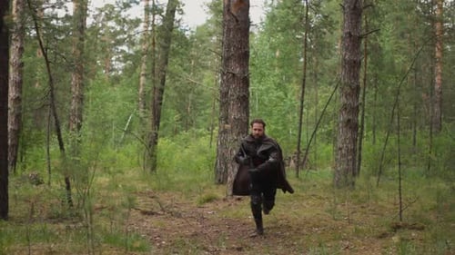 Medieval Warrior with Cape and Large Sword Runs Across Wood