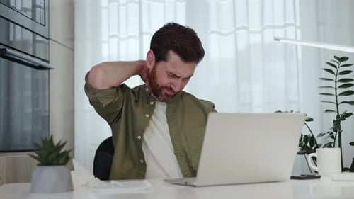 Bearded Man Massaging Stiff Neck at Desk