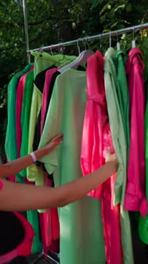 At the Summer Park Fair a Young Girl is Choosing Colorful Clothing at a Booth