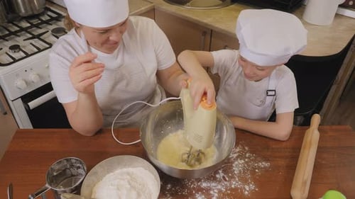 A Cute Boy in an Apron and a Cap Beats Dough for Cookies on His Own with a Mixer