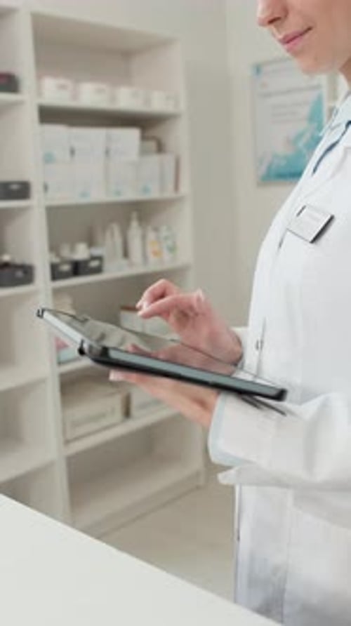 Close Up Pharmacist using Tablet in Pharmacy Vertical