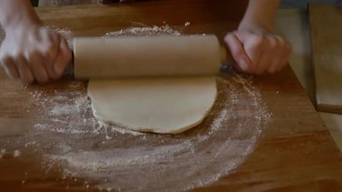 Hands Flatten Dough with Rolling Pin on Cutting Board