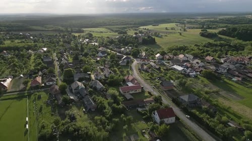 Luftaufnahme eines kleinen Dorfes bei Sonnenuntergang, umgeben von Feldern und Wäldern