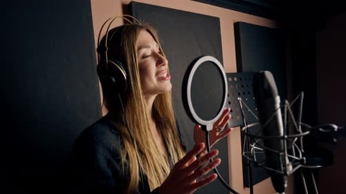 girl singer singing in a recording studio with headphones in front of microphone to create a song