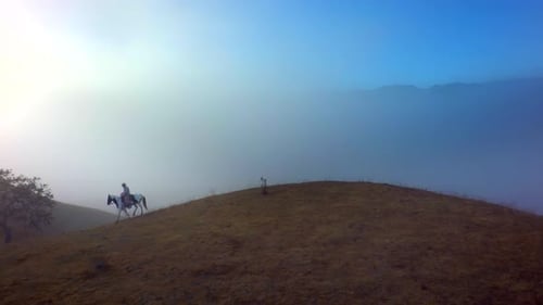 Cowboy on Horseback Riding Across Misty Hill