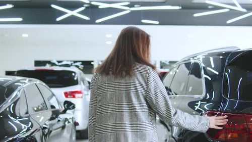 Woman in a Stylish Coat Enters a Luxury Vehicle in an Upscale Car Dealership During the Afternoon