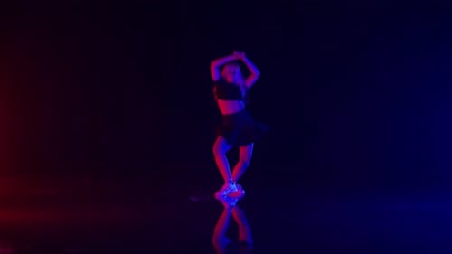 Young Woman with Long Blond Hairs Dances in Colorful Stage Lights in Studio