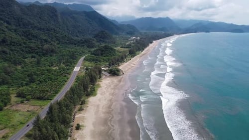 Aerial view of tropical beach and turquoise sea water with small waves close to green mountains.