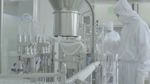 À l'intérieur de la chaîne de production de l'usine, des travailleurs vêtus de blouses de laboratoire et de masques assurent la qualité