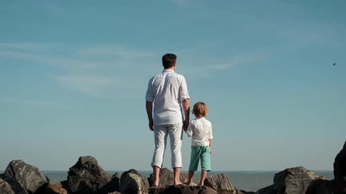 Father and Son Stand on the Edge of a Cliff and Look at the Ocean